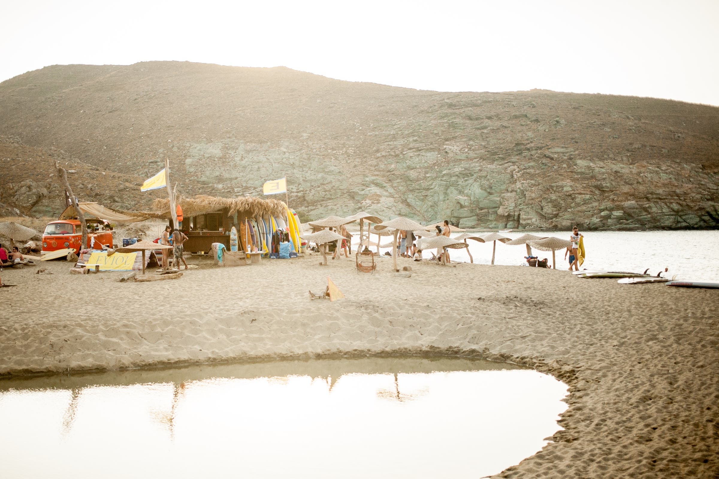 People on a hippie beach with surfers and van in Tinos Island, Cyclades, Greece, representing one of the many outdoor adventures to be had