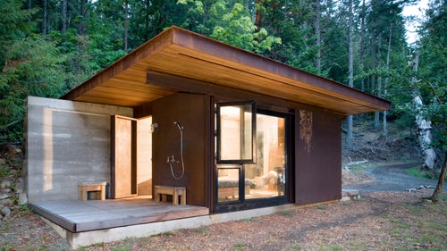 Set on a small island just off Vancouver, the cabin covers the basic necessities of living: a small and efficient wood stove heats a room that contains a bed, kitchenette, and toilet. The steel cladding weathers naturally and will eventually blend in with the surrounding rocks and foliage. Interior surfaces are primarily made from a demolished local bridge and cedar harvested from fallen logs on the property.