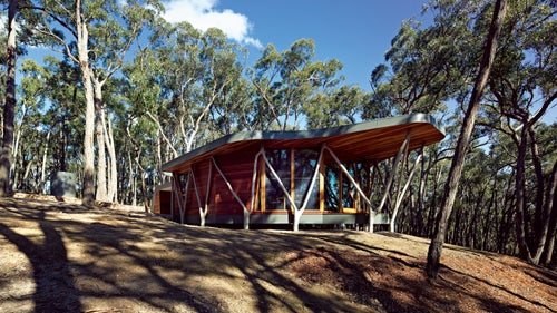 The structure fits its surroundings effortlessly, as forked tree branches appear to grow out of the ground to support the building. Bringing together components of the small Australian house, the primitive hut, and traditional Aboriginal structures, this home allows those inside to take in the picturesque setting.