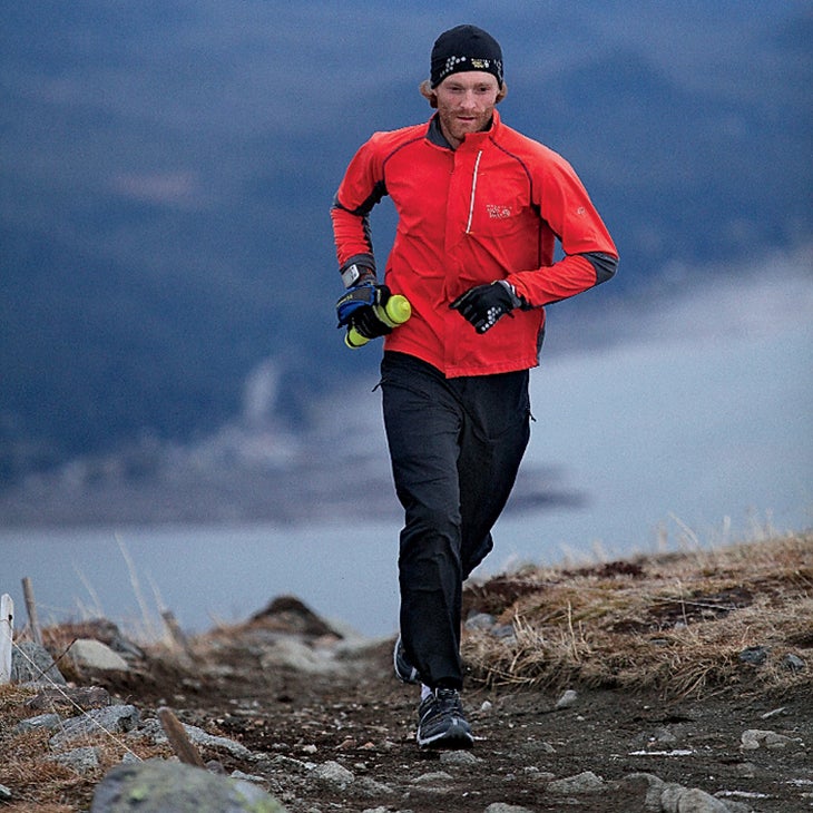 Geoff Roes running a dirt trail in a red jacket and black pants