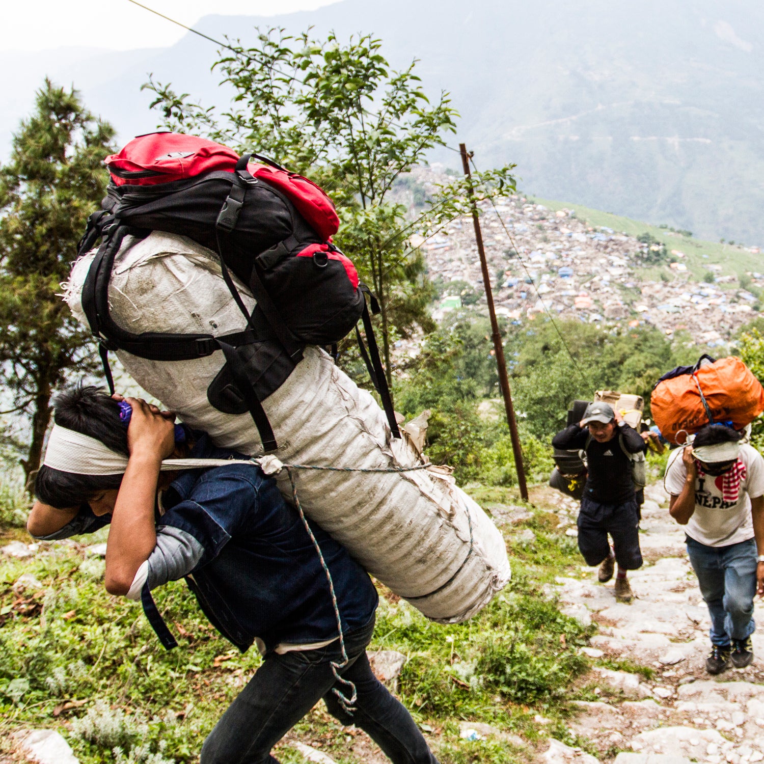 Barpak, Gorkha District Nepal.Thirty-six porters hired by Oxfam to deliver relief material by foot to the remote village of Laprak, becuase the road is inaccessible due to recent landslides. The village of Barpak can clearly be seen in the background. Distribution coverage: 642 Households