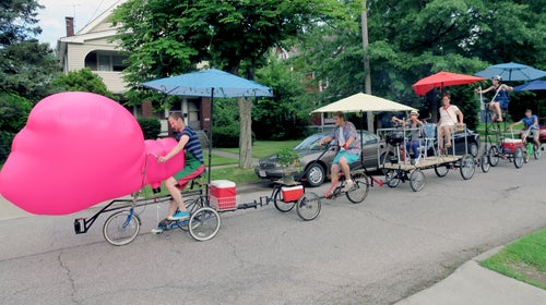 Artist Jimmy Kuehnle (front bike) rides the swing bike he built to hold coolers of beer, a grill, and 
