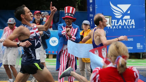 Scott Overall hits the tape, right,  to win the men’s open division while runner Ben Payne comes in second place at the finish line of the AJC Peachtree Road Race on July 4, 2015.
