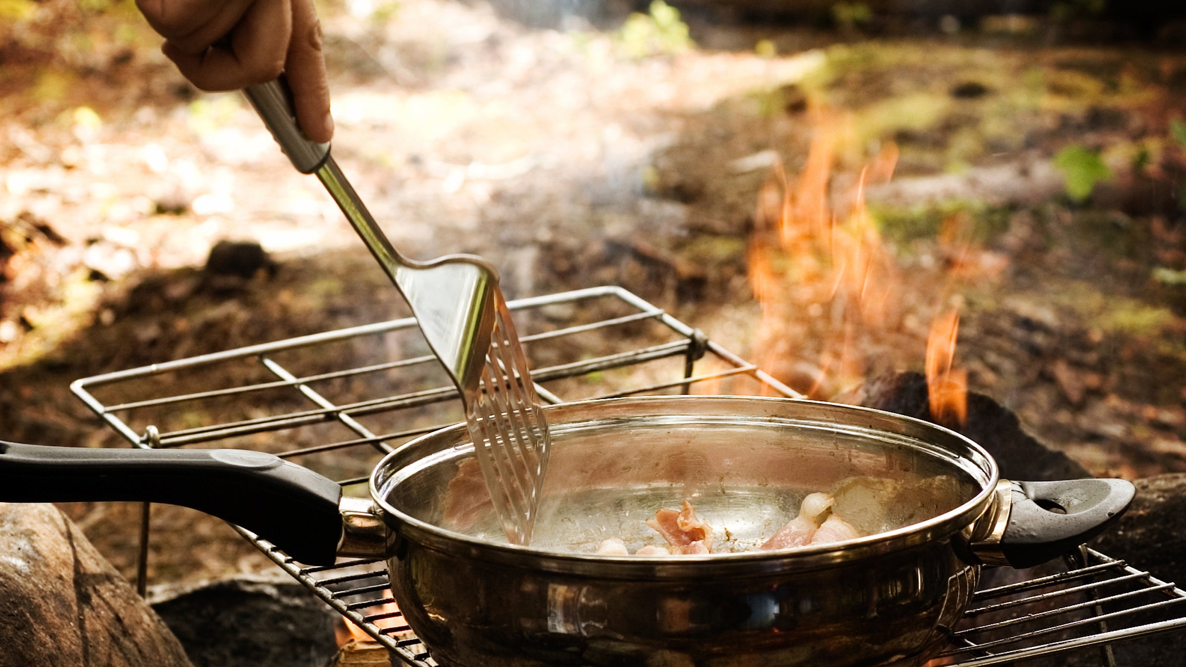 cooking a pan of bacon over a grill outside