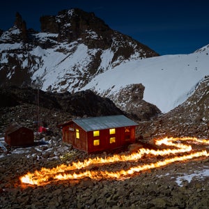With petroleum as his paint, English photographer Simon Norfolk took to Africa’s second highest peak, Mount Kenya, to outline the mountains’ vanishing Lewis Glacier. Using old maps and meticulous GPS plotting, the fire lines represent an old section of the glacier, often a large distance from the glacier’s current front. Norfolk’s work, completed in 2014, is marked by grief but he hopes it also serves as a call to action. In his words, to think that “in ten or twelve years this magnificent glacier that has endured for millennia will exist only in photographs, is unbearable.”
Photo: Norfolk was born in 1963, the year of the glacier’s position depicted by this fire line. At that time only the small hut on the left existed. The larger structure with the lights on, called the Austrian Hut, was built in 1972 and served as Norfolk’s residence during this project in 2014.