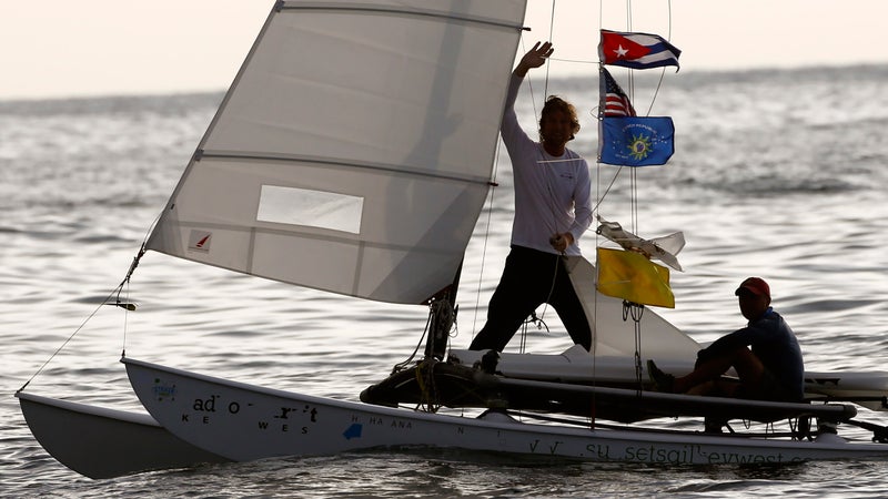 Second-place sailor Seth Salzmann waves alongside teammate Wade Miller on their catamaran decorated with Cuban and U.S. flags as they arrive from Key West, Florida, to the Marina Hemingway.