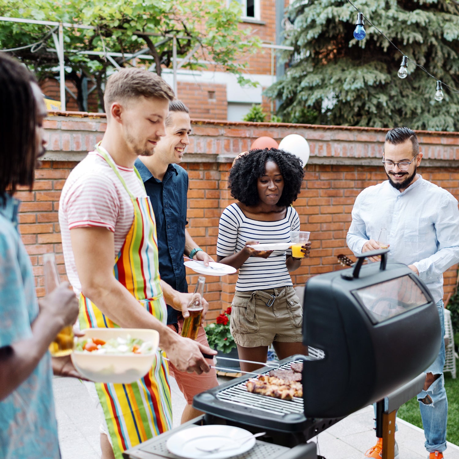 Group of cheerful young people eating an d drinking at barbecue party in a backyard.