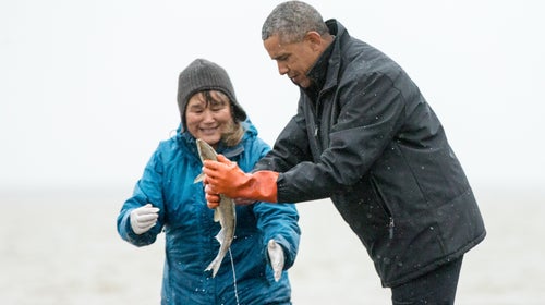 President Obama reacts as a fish he is holding releases milt, the sperm-containing fluid of a male fish, while visiting with Commercial and Subsistence Fisher Kim Williams in Dillingham, Alaska.