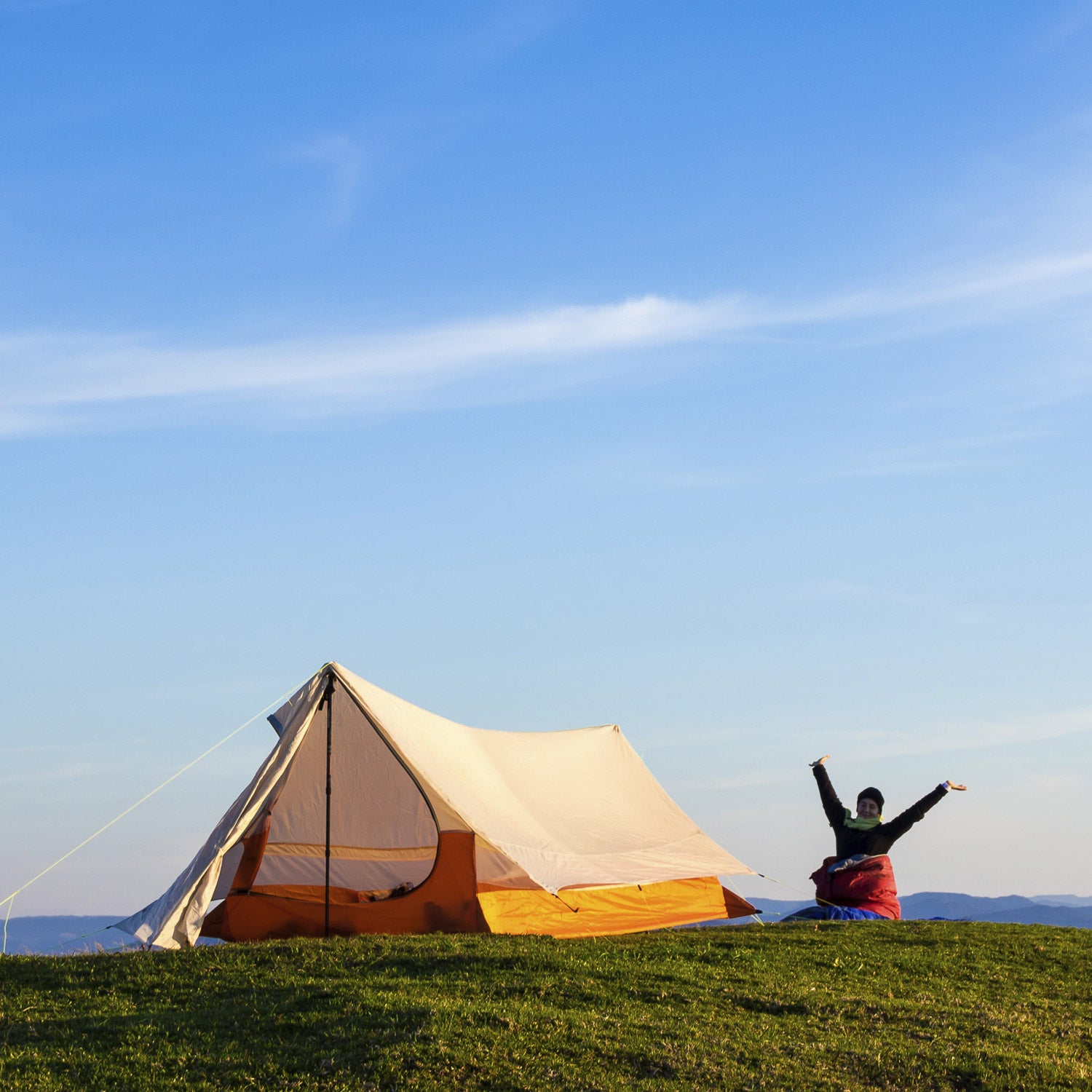 Woman Waking up with the arms up in the air after a night on the top of a Mountain