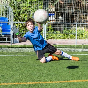 Young football goalkeeper stretching to stop a ball