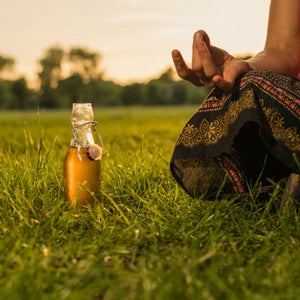 A young woman is meditating in a park at sunset, there is a bottle of health drink next to her