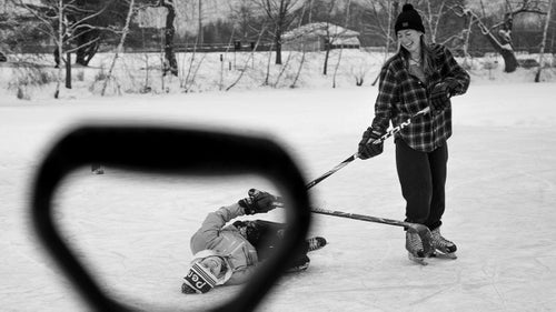 Two Colby students are shown through the handle of a shovel used to clear the ice. Though the game was competitive, the atmosphere was decidedly lighthearted. “The whole point was to balance the teams and just try to get the level of the game as high as possible,” Wynia says. “It seemed to be a battle against winter—getting your heart rate up on a freezing afternoon—more than anything.”
