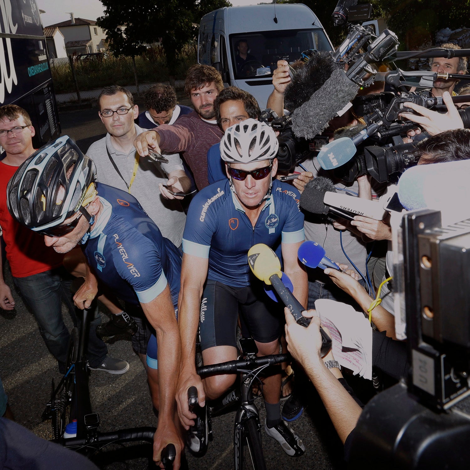 Lance Armstrong, center, rides through journalists while being surrounded by the media as he joins former England footballer Geoff Thomas and his team of ten amateur riders for two stages of the 