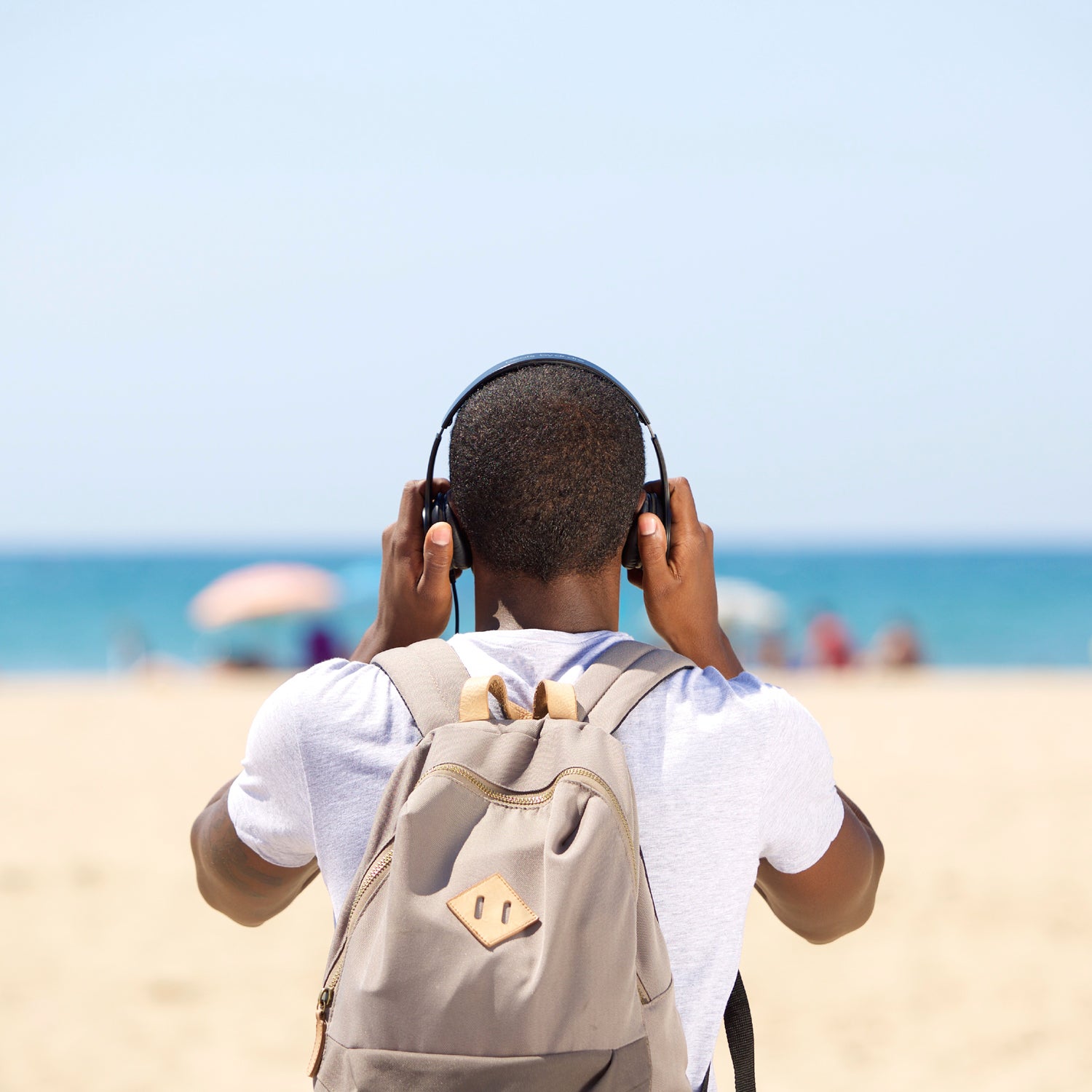 Young man with headphones and bag standing at the beach from behind