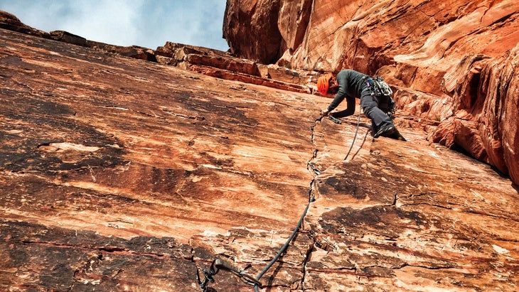 man in orange helmet climbs trad route up a crack on red rock