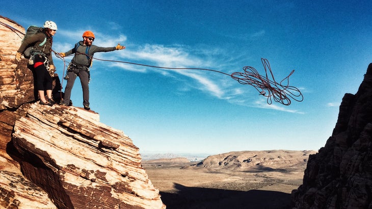 man in orange helmet throws a rope for a rappel against a blue sky