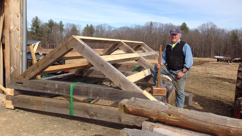 Elwell stands beside the cabin's roof frame, outside his workshop in Ashfield, Massachusetts.