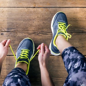 Unrecognizable young runner tying her shoelaces. Studio shot on wooden floor background.