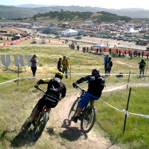 Last weekend, the Sea Otter Classic, an annual event in Monterey, California, that celebrates the arrival of bike season, held the first-ever large-scale eMTB race. Participants rode motorized whips around a 1.5-mile course for 60 minutes and competed either in the men’s (by age), women’s (by age), or industry category. All the bikes had to be pedal-assist (no throttles), with just one battery (no mid-race swaps). Some riders took the event seriously and tried for the win, while others donned costumes and just tried to finish. In the end, Christoph Saucer, a former mountain bike world champion, landed on top of the podium. “It was something completely different,” he says. “It was as hard as any cross-country race I’ve ever done. The pacing is just a little… different.”
Photo: Two riders rip the big S-curve leading into the finishing straight.