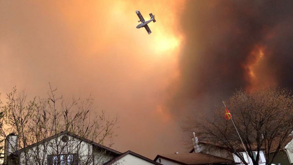 Smoke fills the air as a small plane flies overhead in Fort McMurray, Alberta, Tuesday, May 3, 2016. The entire population of the Canadian oil sands city of Fort McMurray, has been ordered to evacuate as a wildfire whipped by winds engulfed homes and sent ash raining down on residents. 