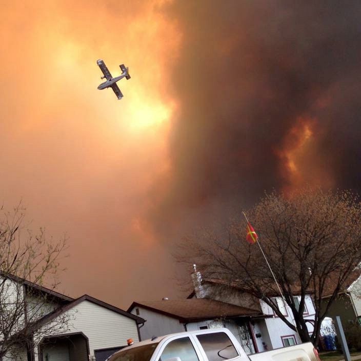 Smoke fills the air as a small plane flies overhead in Fort McMurray, Alberta, Tuesday, May 3, 2016. The entire population of the Canadian oil sands city of Fort McMurray, has been ordered to evacuate as a wildfire whipped by winds engulfed homes and sent ash raining down on residents. (Kitty Cochrane/The Canadian Press via AP) MANDATORY CREDIT