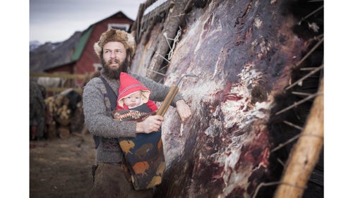 Alex carries his son as he works at fleshing a hide for tanning.