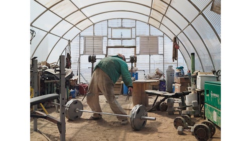 Roger lifting weights; Jonah Natural Gas Field; Boulder, Wyoming, 2010.
Roger is a welder on the Pinedale Anticline and Jonah Field. The presence of natural gas in the area was known for years, but it was not deemed practical to extract with conventional drilling methods. In the 1970s, El Paso Natural Gas Company proposed a project called Wagon Wheel Nuclear Stimulation Project, which was an attempt to detonate nuclear devices to fracture the rock formations and enable natural-gas extraction. The project was abandoned. Today, fracking has made the area one of the most productive in the continental United States.
Roger, a former bodybuilder and U.S. Army Special Forces soldier, regularly lifts weights in the toolshed at work.