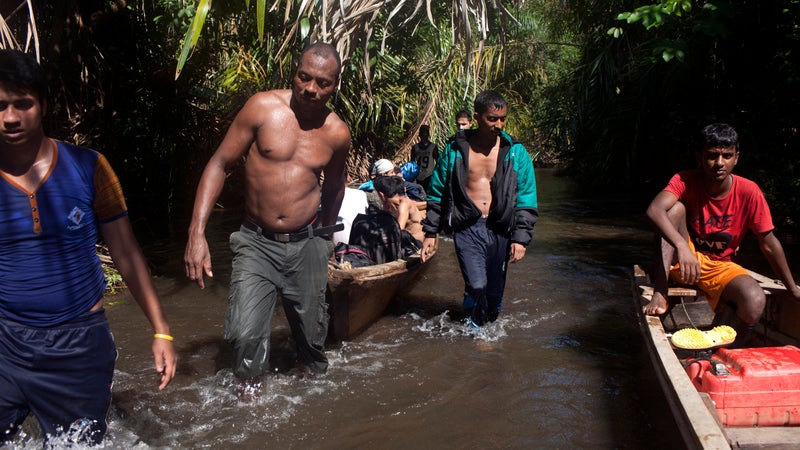 Migrants and coyotes move a boat through shallows.