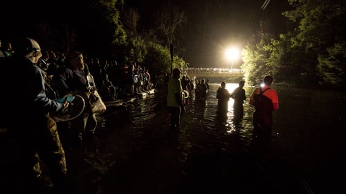 Feeders mingle with spectators as rain begins to fall on the river. Feeders deliver nutrition to teams as they pass by.