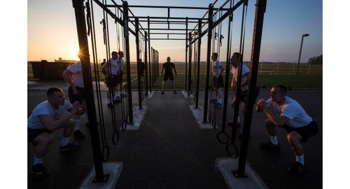 Instructor AST2 Jon Disalle and members of Class 118-16 perform squats in front of the pull-up rack.