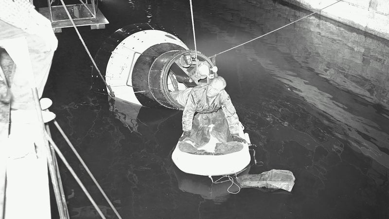 Astronaut John H. Glenn Jr., pilot of the Mercury Atlas 6 spaceflight, emerges from an egress trainer during training activity at the Langley Research Center. He is attempting to transfer onto a life raft from the mock-up of the Mercury capsule.