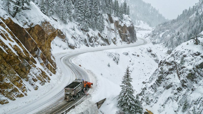 A snowplow pushes snow off the edge as it makes it's way through the canyon.