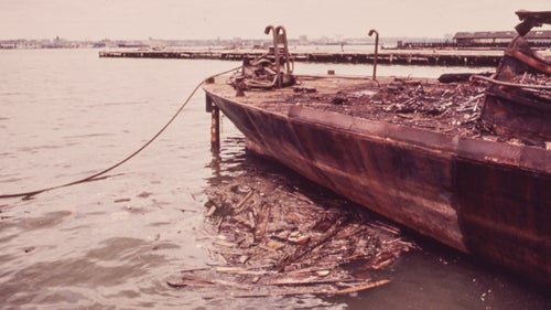 A rusting barge deposits debris in the Hudson River near the newly built World Trade Center in Lower Manhattan, 1973.
