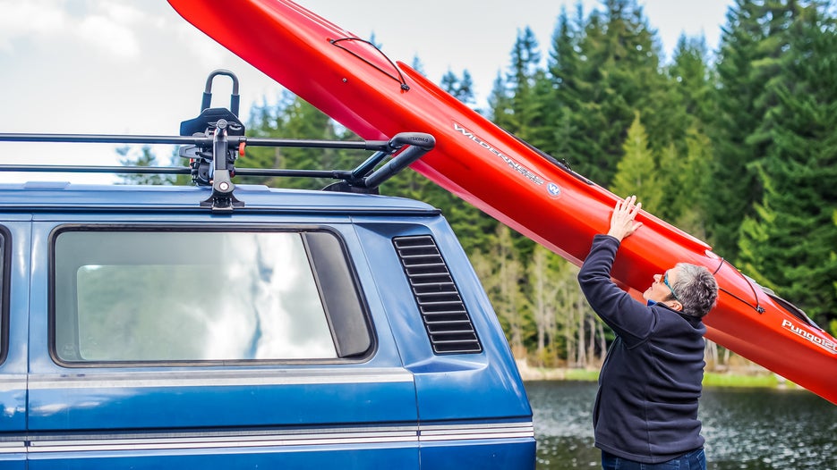 A woman loads her kayak onto her vehicle, using Yakima's ShowBoat—a load-assist boat carrier.
