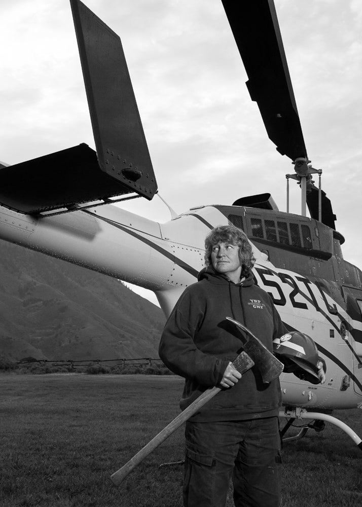 Wendy holding an axe in front of a helicopter. The dispatcher’s primary job is communicating during fire support and search and rescue operations.