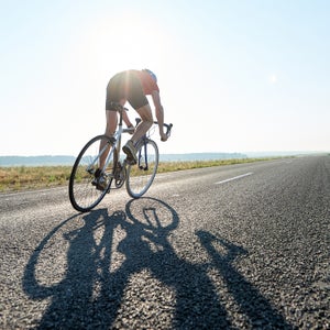 Rear view of sportsman riding bike on roar in sunlight, he participating in competition
