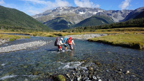 Hiking partners cross a stream near Nelson Lakes, New Zealand.