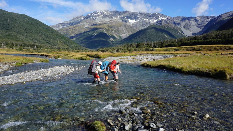 Hiking partners cross a stream near Nelson Lakes, New Zealand.