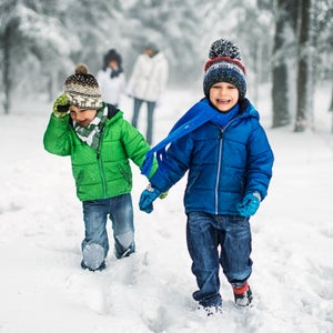 Mother and three kids having fun in forest on snowy day. Girl is aged 9 and boys are aged 6. The laughing boys are running in front and the mother with daughter is walking in the background. It's snowing on cold winter day.