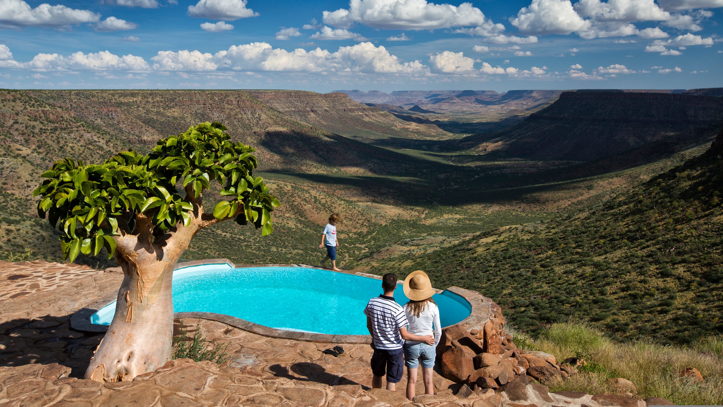 A couple stands at the Grootberg Lodge swimming pool looking out into the Klip River Valley, Damaraland, Namibia.