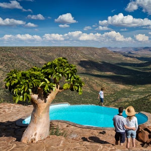 A couple stands at the Grootberg Lodge swimming pool looking out into the Klip River Valley, Damaraland, Namibia.