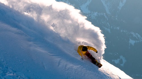 A snowboarder throws some spray during magic hour in the Whistler backcountry, BC, Canada.