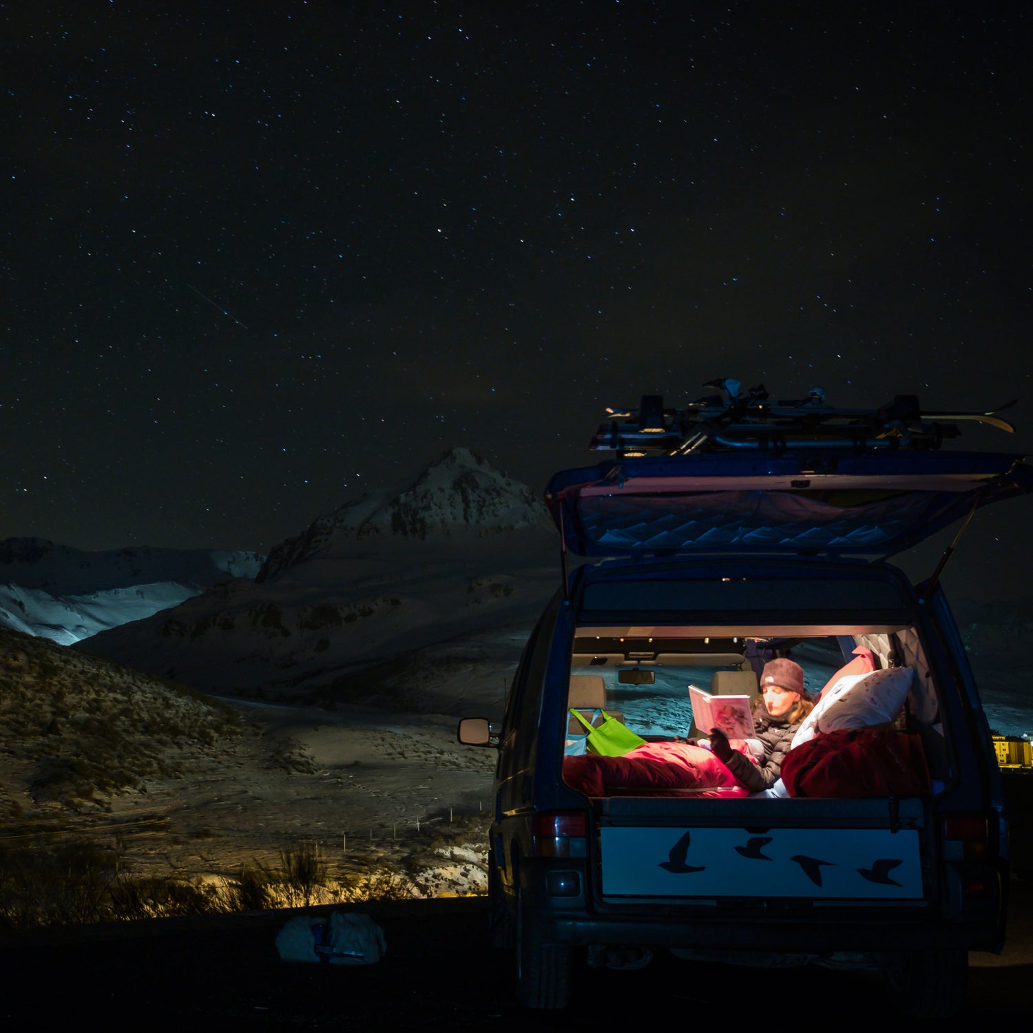 Chica viajando en furgoneta pasando noche bajo estrellas en invierno, tapada con un saco de dormir.