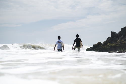 Alongside a government-constructed breakwall two of Mahabalipuram's younger surfers walk towards a sandbank formed by the breakwall beside them before jumping out to surf. On big days a strong current sweeps down the beach from South to North and with the difficult paddle many of the local surfers have perfected a formidable rock dance to jump out right at the top of the point where the breakwater juts out.