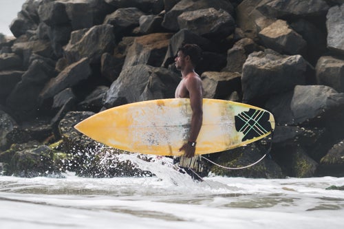 Raghul Paneerselvam, a local 26yr old surfboard shaper and ding repair master, walks next to a breakwater before jumping out into a day of solid waves. The breakwater was put in place by the Indian government to protect against erosion that was threatening a UNESCO world heritage site behind it. The site, a series of sanctuaries from the 7th and 8th century Pallava dynasty, draws throngs of domestic and international tourists. The breakwater also helped in creating one of India’s best waves.