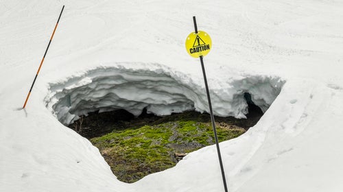 Caution sign warning skiers and snowboarders of a large hole caused by melting snow.