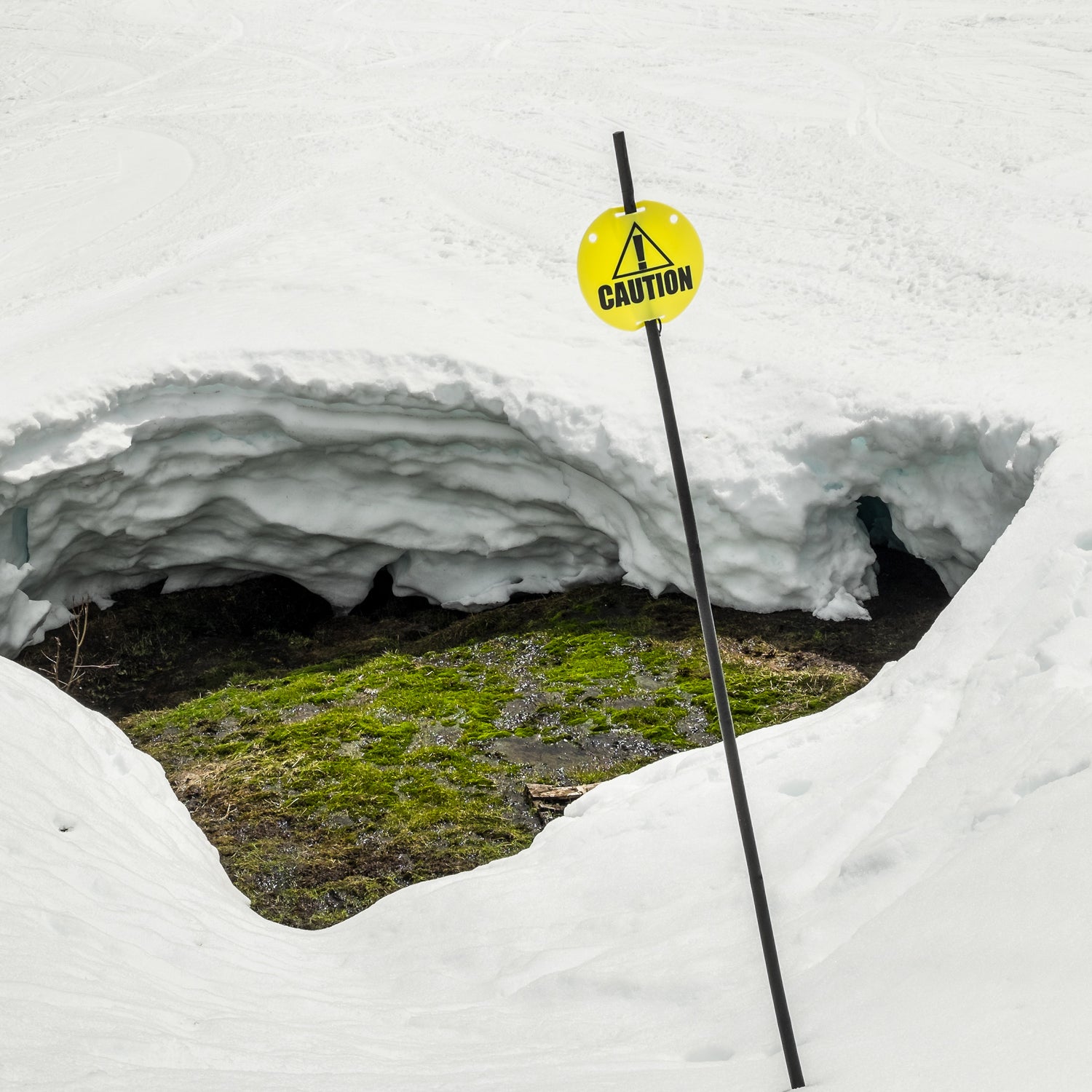 Caution sign warning skiers and snowboarders of a large hole caused by melting snow.