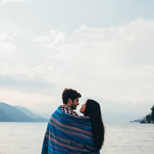 Couple wrapped in blanket standing by the lake