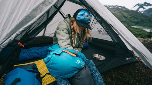 Woman stuffing sleeping bag into stuff sack in tent