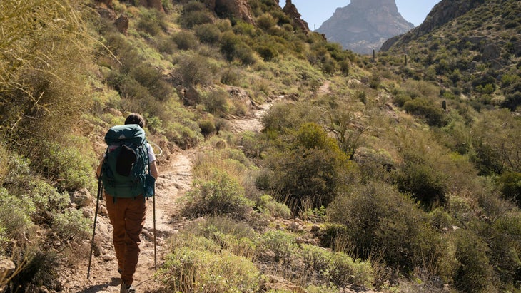 person hiking up singletrack in desert with mountain in the back